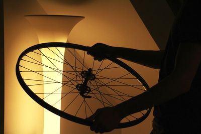 Midsection of man holding bicycle spoke by illuminated lamp shade