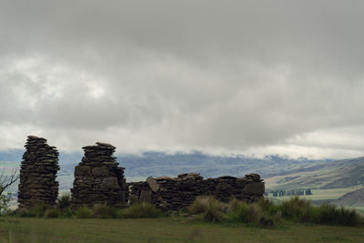 Stack of rocks on field against cloudy sky