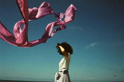 Woman standing by pink flowers against blue sky