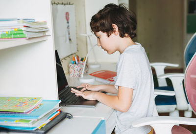 Tween boy do homework learn foreign language writing in pupil book with opened laptop at the room 