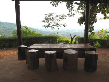 Table and chairs by trees against sky