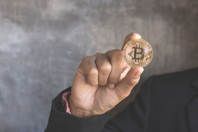 Cropped hands of business person holding bitcoin against wall