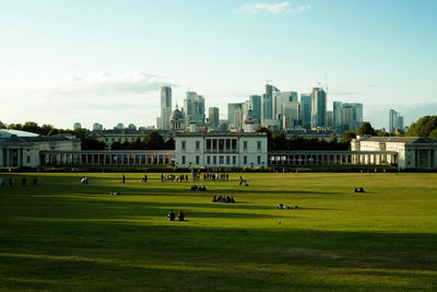 Group of people on field by buildings against sky