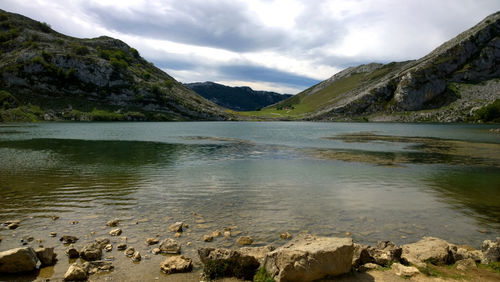 Scenic view of lake enol by mountains against sky