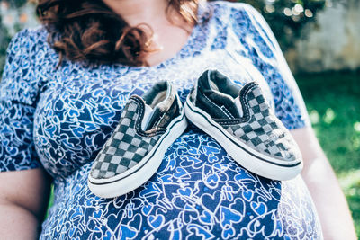 Close-up midsection of pregnant woman with shoes on abdomen