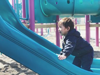 Side view of boy standing on slide at playground