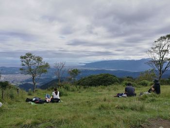 People relaxing on field against sky