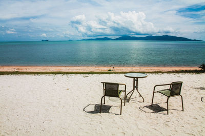 Empty chairs on beach against sky