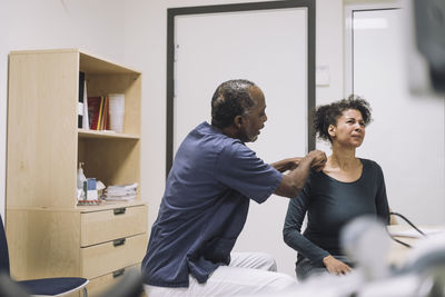 Male healthcare worker examining shoulder female patient grimacing with pain in medical clinic