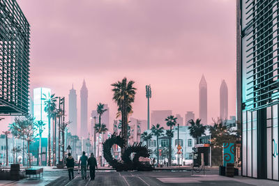 People walking on road by buildings against sky