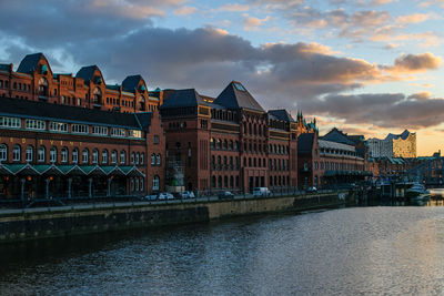 Buildings by river against cloudy sky