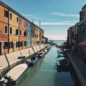 Boats moored in canal by buildings against sky