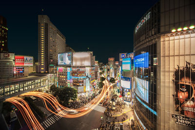 High angle view of illuminated street by buildings against sky at night