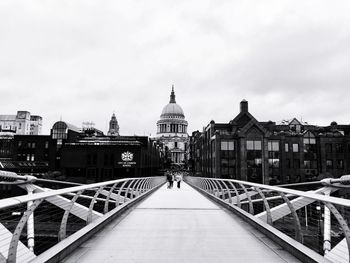 Footbridge over canal amidst buildings against sky in city