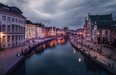 Canal amidst illuminated city buildings against sky