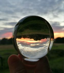 Close-up of hand holding crystal ball against sky during sunset