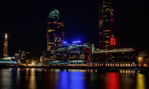 Illuminated buildings by river against sky at night