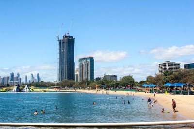 People on beach by city against sky