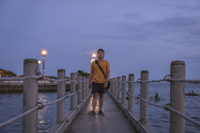 Rear view of man standing on pier by sea against sky