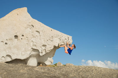 Woman climbing rock against clear blue sky