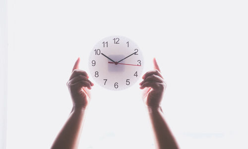 Cropped image of person holding clock against white background