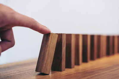 Cropped finger of person touching wooden domino on table against white background