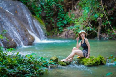 Young woman sitting on rock by waterfall