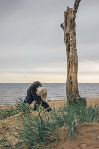 Young woman exercising while crouching by tree trunk at beach