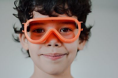 Close-up portrait of boy wearing orange goggles against wall