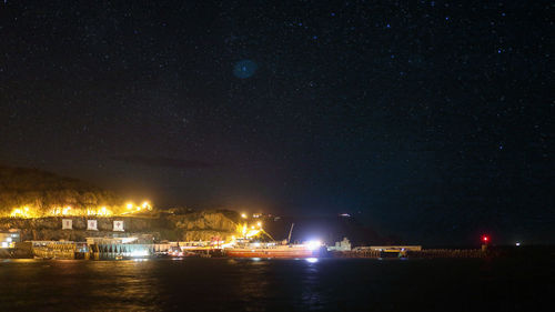 Illuminated city by sea against sky at night