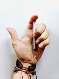 Close-up of man hand holding syringe over white background