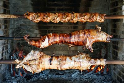 Pork on metallic rod hanging against barbecue