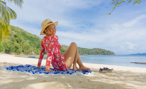 Woman sitting on beach by sea against sky