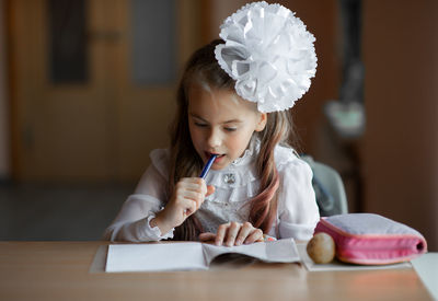 Cute girl studying while sitting by table at home