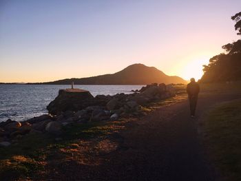 Silhouette people standing on rock by sea against clear sky during sunset