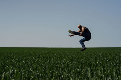 Full length of bald man kicking in mid-air over agricultural field