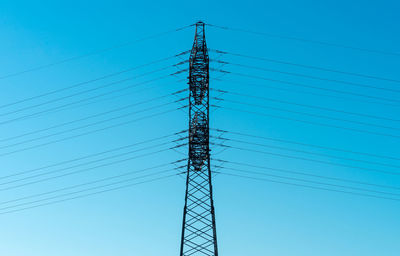 Low angle view of electricity pylon against clear blue sky