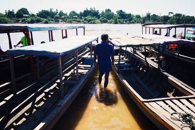 Rear view of man standing amidst boats moored in river