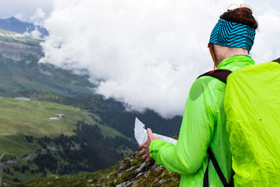 Rear view of hiker looking at map against clouds over landscape