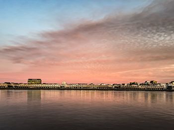 Scenic view of river by building against sky during sunset