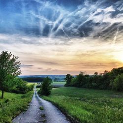 Empty road amidst field against sky during sunset
