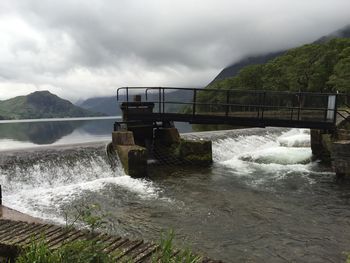 Water flowing on dam by river against sky