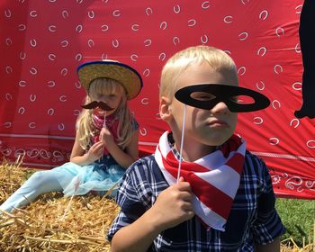 Playful siblings holding props while sitting on grassy field