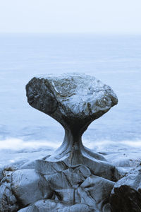 Rock formation in sea against sky during winter