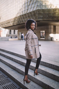 Beautiful african american young woman with afro in a stylish coat, smiling. urban street portrait