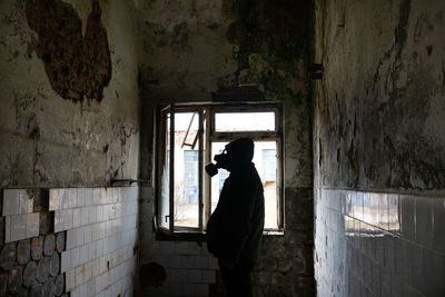 Side view of silhouette man wearing gas mask standing in abandoned house