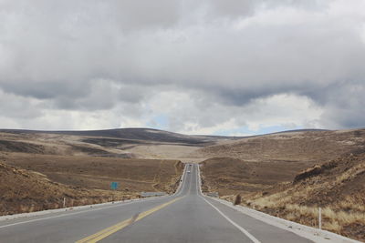 Empty road leading towards mountains against sky