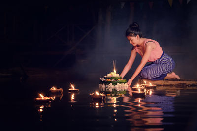 Young woman in traditional clothing kneeling by lake at night