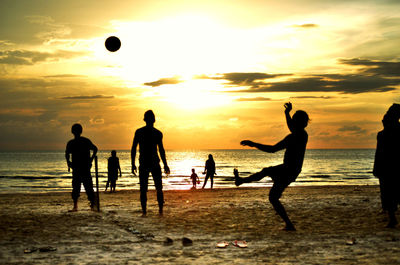 Silhouette people playing soccer at beach during sunset