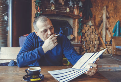 Mature man smoking cigarette while reading file at home